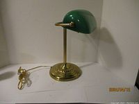 Side view of bankers lamp showing green glass shade and brass base with attached power cord.