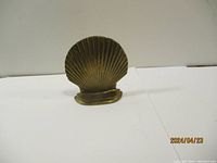 Front view of one brass shell door stop showing scalloped shell design and flat base