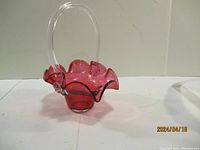 Front angle view of cranberry glass basket showing ruffled edge and clear glass handle