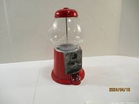 Front and side view of red metal gumball machine with clear glass globe and coin turn knob.