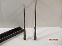 Two Harry Potter collectible wands standing upright next to a velvet-lined box.