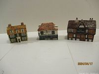 Three ceramic decorative houses lined up on a white surface.