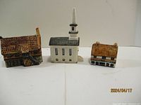 Front view of three ceramic miniature houses: large cottage, church with steeple, and small cottage with beige roof