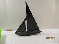 Front angle of black metal sailboat sculpture showing the sail and hull profile.