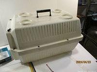 Side view of beige plastic pet carrier showing ventilation slits, circular holders on top, and black handle.