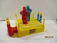 Red and blue robots inside the yellow boxing ring with ropes and corner posts visible