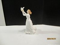 Side angle view of the Royal Doulton porcelain figurine "Thinking of You" showing a woman in a flowing dress holding two doves up in the air.