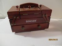 Front view of closed Singer wooden sewing box with four small knobs and a handle on top.