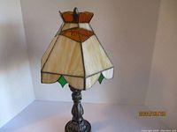 Tiffany style stained glass table lamp shown unlit, highlighting the cream, orange, and green stained glass shade and detailed dark metal base.