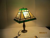 Photo of the Tiffany style lamp illuminated, showing the stained glass shade with green and beige colors and angel design.