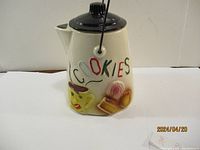 Front view of the ceramic teapot style cookie jar with 'COOKIES' lettered and decorative cookies and bear face design