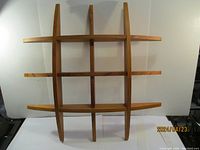 Full front view of a wooden wall shelf with intersecting slats forming square compartments.