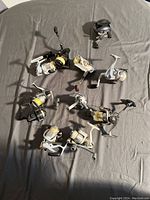11 assorted fishing reels laid out showing variety of colors and sizes.