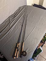 Fishing rods laid out on a grey fabric surface, showing cork and synthetic handles, some with reel attached.
