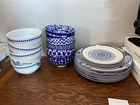 Stack of blue and white bowls, side plates, and dinner plates arranged on a wooden surface against a white wall