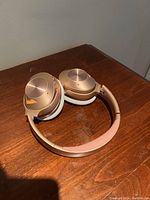 Rose gold over-ear headphones folded and resting on a wooden surface, showing the exterior of ear cups.