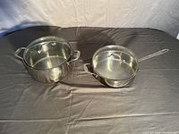 Photo showing the large stockpot and large saucepan without lids on a gray surface with cloth background.
