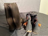 Two pairs of fishing shoes, tall rubber boots and ankle-high zipper shoes with fabric upper, viewed from back side showing sole and heel.