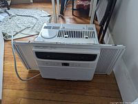 Front view of the white Frigidaire air conditioner with side panels extended and power cord visible on wooden floor