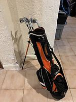 Orange and black stand golf bag standing with telescoping legs deployed