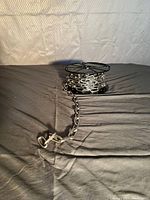 Heavy metal chain coiled on a black plastic spool, with the chain extending outwards showing the hook clasp end.