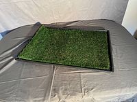 Artificial grass relief mat on black tray placed on gray surface, viewed slightly from side angle.