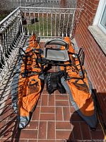Full overview of two orange pontoons, black support frame, seat, side bags and measuring net arranged on patio floor