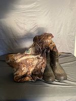 Waders and boots folded on a gray surface, showing camo pattern and attached boots.