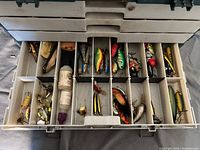Top tray of the tackle box showing a variety of colorful fishing lures, a small bottle, and some miscellaneous small items.