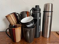 Photo showing all ceramic mugs stacked and travel mugs standing upright on right
