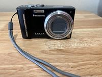 Front view of Panasonic Lumix digital camera showing Leica lens and wrist strap on wooden surface