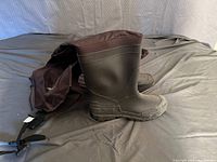 Photo showing the full pair of dark brown pull up leg waders laid out with boot bottoms and legs visible on a black surface.