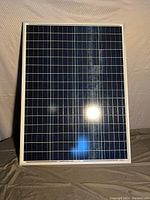 Front view of NewPowa 100 watt solar panel showing blue photovoltaic cells and white frame.