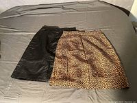 Two vintage pencil skirts laid flat on a bed, one black leather and one leopard print fabric.