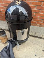 Weber black charcoal smoker assembled and standing upright showing smoker door and vent on lid.