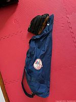 Blue New York Yankees bat bag with attached shoulder strap, displayed on red foam floor mat