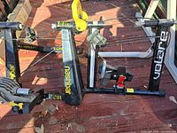 Photo showing two folded bicycle exercise stands placed on outdoor surface with Nashbar and Volare logos visible