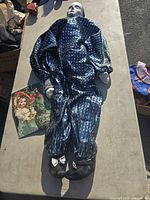 Porcelain doll lying on table, wearing blue patterned outfit and black shoes with white bows, calendar beside doll.