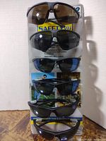 Six pairs of dark tinted SafetyVu industrial safety sunglasses displayed vertically with branded packaging showing safety standard compliance