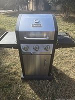Front view of stainless steel Dyna-Glo propane gas grill with lid closed and three control knobs.
