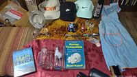Photo showing multiple items on a red table runner including hats, glasses, books, DVDs, apron, and decorative items