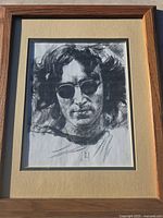 Close-up photo of the framed ink drawing of John Lennon showing detailed facial features and sunglasses.