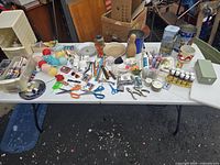 Full view of table with assorted crafts supplies including scissors, buttons, paints, brushes, glue, decorative ceramic items