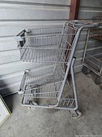 Side view of the small metal grocery cart showing two wire baskets and wheels.