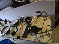 Photo showing various electronic and household items on a table including clocks, keyboard, fireplace brush, desk spotlight, and other parts.