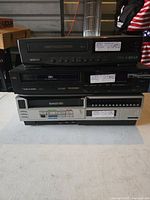 Stacked view of three VHS players: Samsung on top, Realistic in the middle, Panasonic at bottom.
