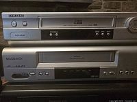 Photo showing Samsung and Magnavox VHS players stacked, details of front panels visible