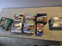 Lot of 8 assorted jigsaw puzzles laid out on a table showing box artwork and puzzle piece counts