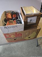 Box lot of assorted items including vintage flashlights, Fisherbrand boxed items, coiled tubing, and miscellaneous hardware labeled aquarium parts in a Dole banana box.