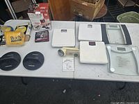 Table displaying all items in the lot including weight scales, push-up bars, handheld massager, and packaged Sears clothes shaver.